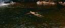 Woman floating on her back in a river pool near a waterfall, relaxing in midlife